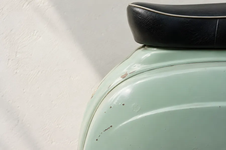 Seitenhaube eines alten Motorrollers in Mintgrün mit kleinen Lackabplatzern, darüber die schwarze Sitzbank